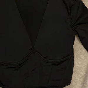 Korsett topp - En lång ärmad svart topp, med djup urringning. Sitter åt och är väldigt smickrande på. Det är ingen riktig korsett utan enbart korsett designad. 