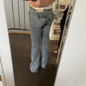 Blå bootcut jeans - Säljer ett par snygga blå bootcut jeans i en klassisk stil. De är lågmidjade och har en lätt slitning framtill som ger en cool look. Perfekta för både vardag och fest!