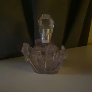 Parfym från Ariana Grande - Säljer en superfin parfym från Ariana Grande. Flaskan är formad som en kristall och har en ljuslila färg. Den har en avtagbar kristallformad hylsa som ger den en lyxig känsla. Perfekt för att ge en touch av glamour till din parfymkollektion!