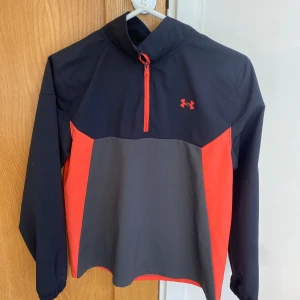 Under Armour golf-vindjacka, i stl  - Jättefin, knappt använd, svart/grå/mörk-orange golf-vindjacka/parka med half-zip, i stl YLG (passar 10-13 åring), Under Armour, nypris ca 850kr, nu endast 500kr! 