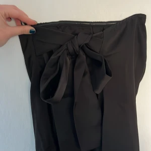 Svart klänning med rosett i ryggen  - En superfin svart klänning med en rosett i ryggen du kan knyta själv. Den är använd en gång tidigare och är därför i mycket bra skick. Den är perfekt när man vill klä upp sig lite till festliga tillfällen! Rosetten i ryggen är en underbar detalj! 🪩🖤🍾