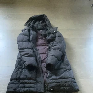 Svart dunjacka från Tommy Hilfiger - Säljer en svart dunjacka från Tommy Hilfiger i storlek M. Jackan är perfekt för kalla vinterdagar med sin tjocka vaddering och långa ärmar. Den har en praktisk huva och stängs med dragkedja. Perfekt för att hålla sig varm och stilren under vintern!