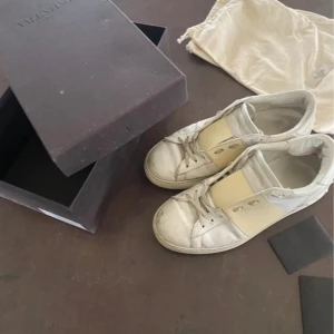 Valentino Garavani sneakers - Säljer ett par snygga Valentino Garavani sneakers i beige och vitt. De har en stilren design med snörning och är i bra skick. Perfekta för både vardag och festliga tillfällen. Kommer med originalkartong. Storlek: 42,5
