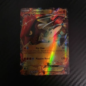 Pokémonkort Groudon EX - Säljer ett Pokémonkort med Groudon EX. Kortet har en holografisk yta som skiftar i regnbågens färger. Det är i bra skick och har attackerna Rip Claw och Massive Rend. Perfekt för samlare eller spelare som vill förstärka sin kortlek!