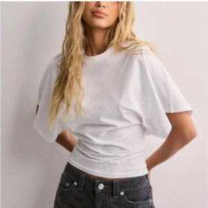 Vit t-shirt - Säljer en stilren vit t-shirt i bomull. Den har en normal passform och korta ärmar, perfekt för vardagsbruk. Enkel och klassisk design som passar till allt. Perfekt för sommaren eller som basplagg året runt.