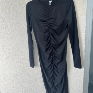 Svart långärmad klänning med rynkdetalj - Snygg svart klänning med långa ärmar och en cool rynkdetalj framtill som ger en smickrande passform. Perfekt för både vardag och fest! Materialet känns mjukt och stretchigt, vilket gör den bekväm att bära hela dagen. Använd endast 1 gång. 