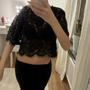 Svart spetsblus - Säljer en elegant svart spetsblus med trekvartsärm. Den är croppad och har ett vackert mönster. Perfekt för festliga tillfällen eller en utekväll. Blusen är i mycket bra skick och passar perfekt till både kjol och byxor.