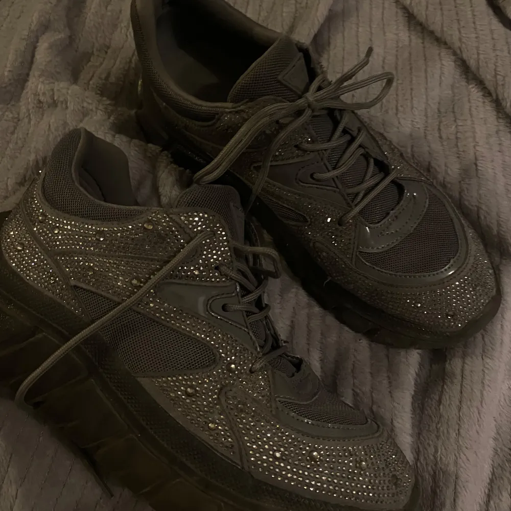 Köptes för 1599kr men säljer för billigare då jag vill bli av med de då jag aldrig använt de. Säljer ett par svarta sneakers från Guess i mycket bra skick. De är täckta med glittriga detaljer som verkligen får dem att sticka ut. Perfekta för att ge din outfit lite extra bling! Skorna har snörning och en bekväm passform.. Kengät.