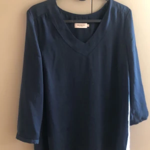 Mörkblå blus från Soaked in Luxury - Säljer en stilren mörkblå blus från Soaked in Luxury. Den har en v-ringad hals och trekvartsärmar, perfekt för både vardag och lite finare tillfällen. 