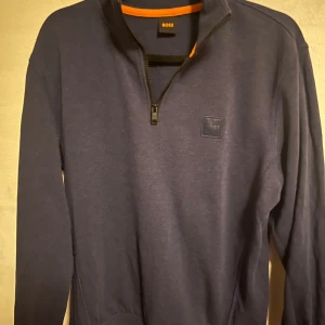 Mörkblå tröja från BOSS - Säljer en stilren mörkblå tröja från BOSS med dragkedja vid halsen. Perfekt för både vardag och lite finare tillfällen. Tröjan har långa ärmar och en diskret logga på bröstet. Passar bra till höst och vår.