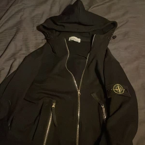 Svart hoodie från Stone Island - Säljer en svart hoodie från Stone Island i bra skick. Den har en dragkedja framtill och två fickor med dragkedjor. M men passar S, qr coden funkar. Äkta!