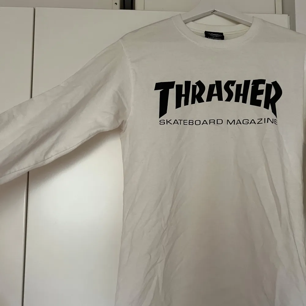 Säljer en vit långärmad tröja från Thrasher med deras ikoniska logga i svart på framsidan. Perfekt för skate-entusiaster eller streetwear-fans. Tröjan är i bra skick och passar perfekt för både vardag och chill. Knappt använd! . Tröjor & Koftor.