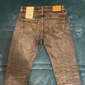 Nudie jeans  - Säljer ett par snygga mörkblåa nudie jeans i nyskick. De har en klassisk femficksdesign med orange sömmar som ger en cool kontrast. Perfekta för både vardag och fest! 🖤 dem är köpta för 1600 och är endast prövade 1 gång men ej använda. Storlek 32 