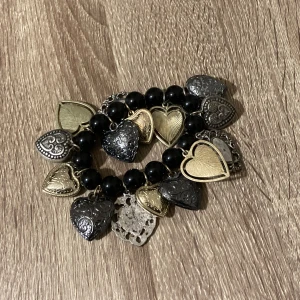  armband med hjärtan - Säljer ett charmigt armband med svarta pärlor och hängande hjärtberlocker i både silver och guld. 