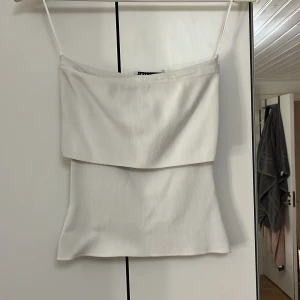 Vit ribbad tubtopp - Säljer en stilren vit ribbad tubtopp i mycket bra skick. Perfekt för sommardagar eller som ett basplagg i garderoben. Den ärmlösa designen gör den lätt att matcha med olika outfits. Passar både till vardags och festliga tillfällen.