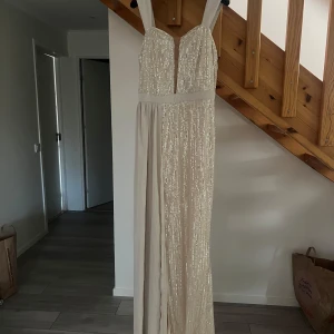 Glittrig långklänning med släp på sidan  - Hej tjejer💕 Säljer en fantastisk glittrig långklänning i champagnefärg. Klänningen har en djup v-ringad urringning och breda axelband. Perfekt för nyår eller fest! ✨