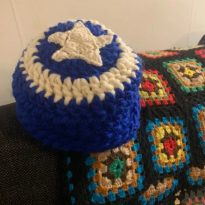 Blå och vit virkad ull mössa med stjärndetalj - Säljer en superfin blå och vit virkad mössa med en cool stjärndetalj på toppen. Perfekt för att hålla värmen under kalla dagar. Den är mjuk och bekväm, och passar perfekt för vintern. Mössan har en härlig blå färg med vita inslag som ger den en unik look. Handgjort och 100% ull!