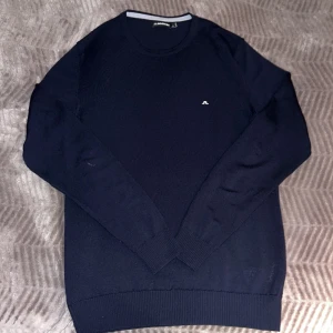 Mörkblå tröja från J.Lindeberg - Säljer en stilren mörkblå tröja från J.Lindeberg. Den har en liten logga på bröstet och är perfekt för både vardag och lite finare tillfällen. Några små tecken på användning finns, men den är fortfarande i suveränt skick.