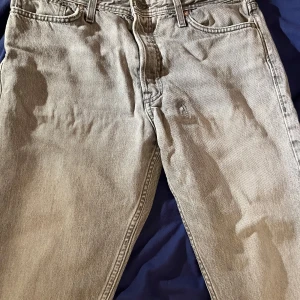 Grå jack&jones jeans - Säljer ett par grå jeansbyxor i bra skick. De har en klassisk femficksdesign och en knappgylf. Perfekta för vardagsbruk och kan enkelt matchas med olika stilar. Passar både till avslappnade och mer uppklädda tillfällen.