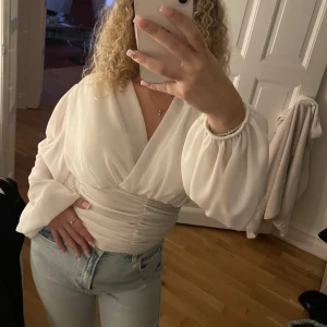 Vit omlottblus - Säljer en superfin vit omlottblus med långa ärmar och puffiga detaljer. Perfekt för både vardag och fest! Helt ny!
