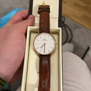 Klocka i bra skick från Daniel Wellington - Säljer en stilren klocka från Daniel Wellington med vit urtavla och brunt läderarmband. Klockan har en elegant guldfärgad boett och minimalistisk design. Perfekt för både vardag och fest! Bra skick säljes med kartong! 450kr Nu sänkt pris 300kr