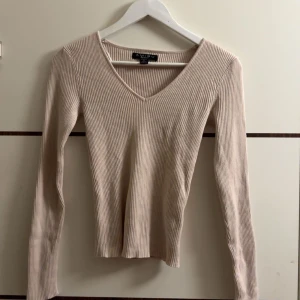 Beige ribbad tröja från Zara - Säljer en superfin beige ribbad tröja från Amisu. Den har en snygg v-ringning och långa ärmar, perfekt för både vardag och fest. Tröjan är i bra skick och passar perfekt till höst- och våroutfits. Den är tight och framhäver figuren på ett snyggt sätt.