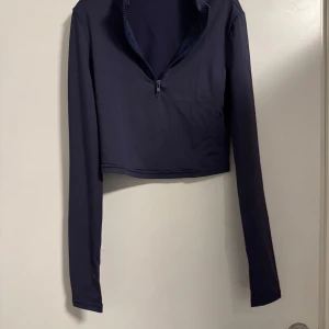 Marinblå idrottströja med dragkedja - Säljer en marinblå träningströja med lång ärm och dragkedja framtill. Perfekt för en casual look eller träning. Materialet känns mjukt och stretchigt, vilket gör den bekväm att bära. Passar bra till både jeans och leggings!