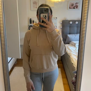 Beige hoodie - Säljer en supermysig beige hoodie i bra skick. Den har en klassisk känguruficka och justerbar huva med snören. Perfekt för höst och vår när man vill ha något bekvämt och stilrent. Passar till det mesta och är ett måste i garderoben! Passar både Xs och S. 