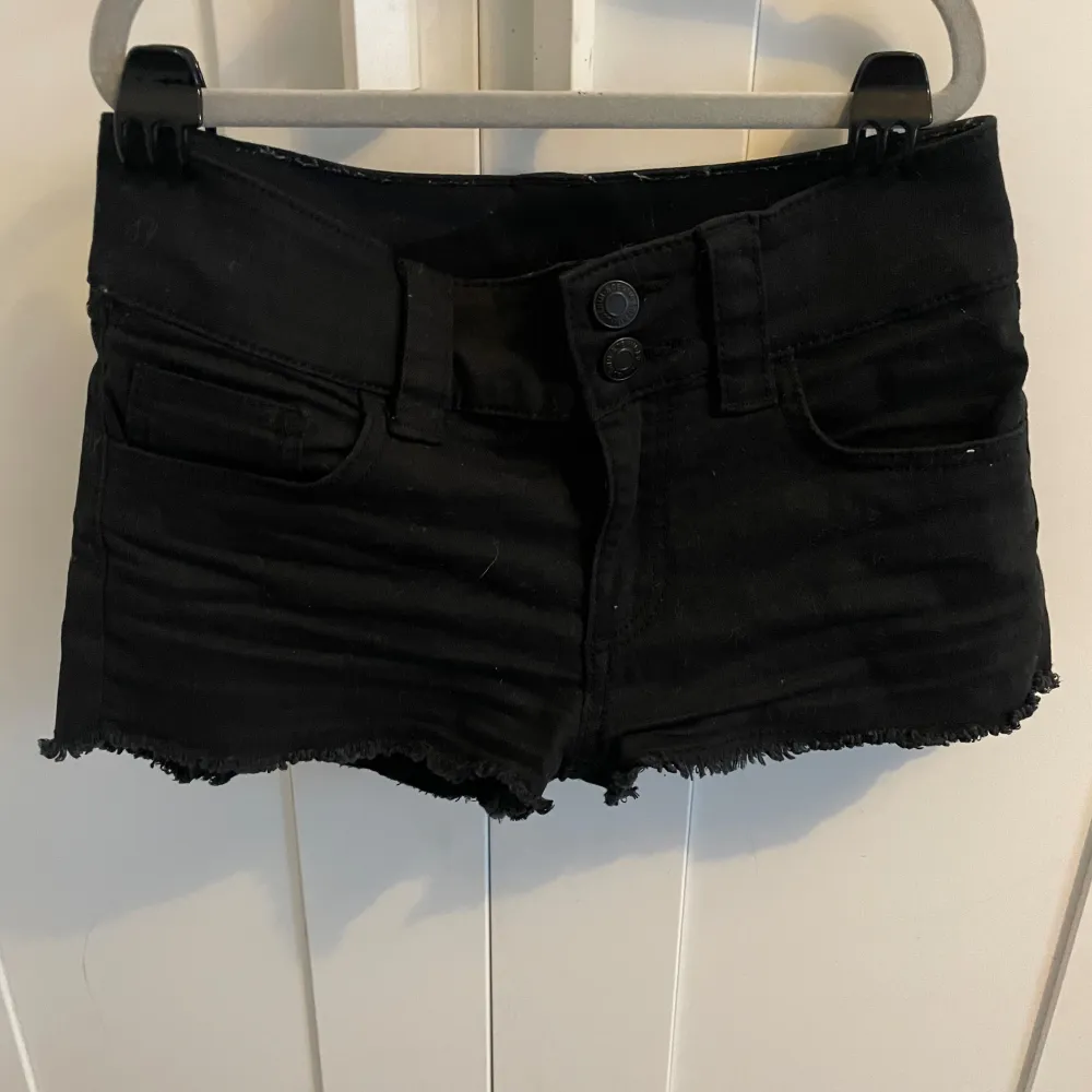 Säljer ett par svarta jeansshorts i bra skick. De är lågmidjade med råa kanter och har två knappar fram. Perfekta för sommarens alla äventyr! 🖤. Shorts.