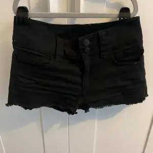 Säljer ett par svarta jeansshorts i bra skick. De är lågmidjade med råa kanter och har två knappar fram. Perfekta för sommarens alla äventyr! 🖤