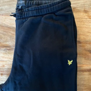 Svarta mjukisbyxor från Lyle & Scott - Säljer ett par svarta mjukisbyxor från Lyle & Scott i mycket bra skick. Aldrig använda. De har en elastisk midja med snörning och en liten gul logga på sidan. Perfekta för en avslappnad dag hemma eller en promenad i parken.