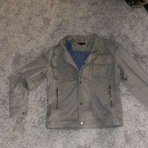 Grå jacka från Dressmann - Säljer en grå jacka från Dressmann i storlek S. Jackan har en stilren design med dragkedja och knappar framtill. Den har två bröstfickor och två sidofickor med dragkedjor. Perfekt för vår och höst! Ifall ni har frågor är det bara att skriva!!!