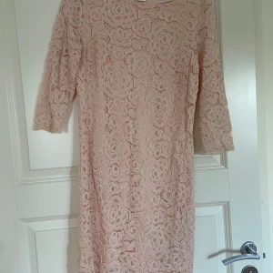 Aprikos spetsklänning  - Säljer en elegant beige spetsklänning med trekvartsärm. Perfekt för vårens och sommarens fester. Klänningen har en vacker blommig spetsdesign som ger en romantisk känsla. Passar bra till både vardag och festliga tillfällen.