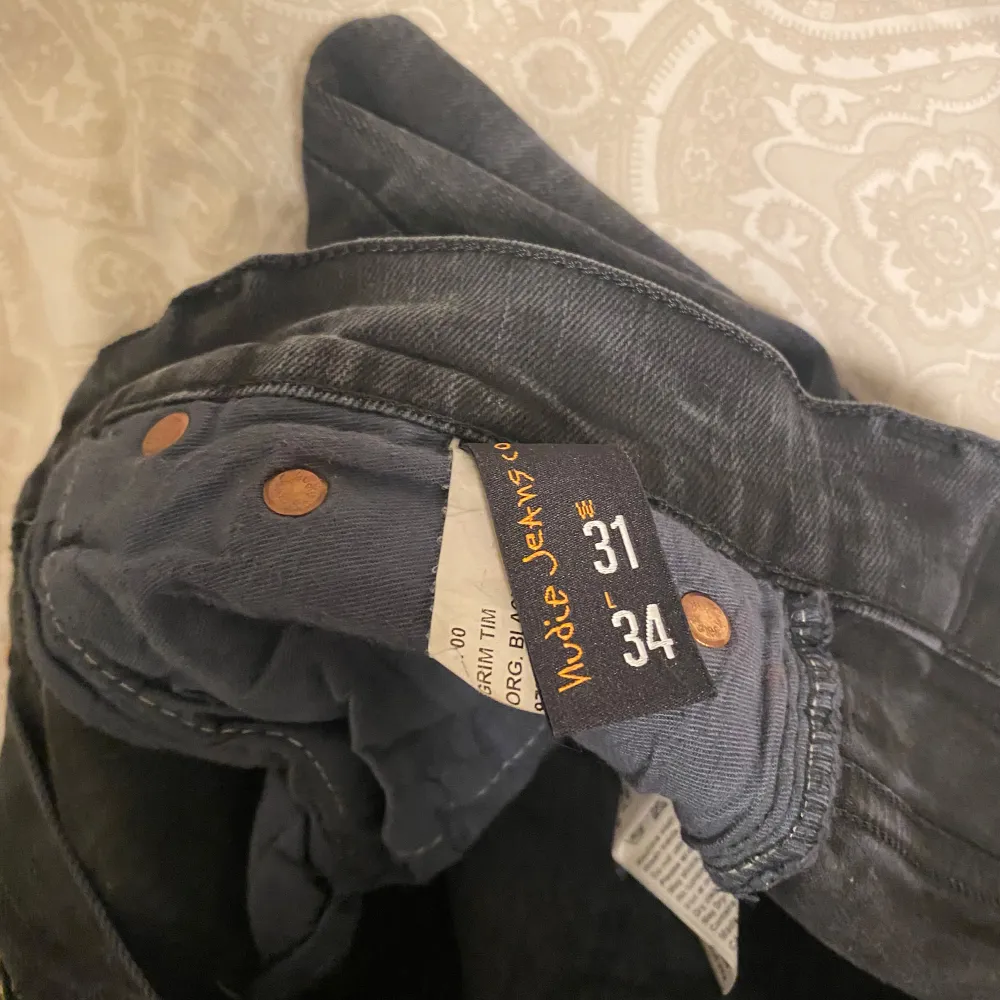 Säljer ett par svarta jeans från Nudie Jeans i storlek 31/34. De har en klassisk femficksdesign med knappar i gylfen. Jeansen är i bra skick och passar perfekt för både vardag och fest. De är tillverkade i slitstarkt denim och har en snygg, mörk tvätt. Modell Grim Tim, nypris 1600kr.. Jeans & Byxor.