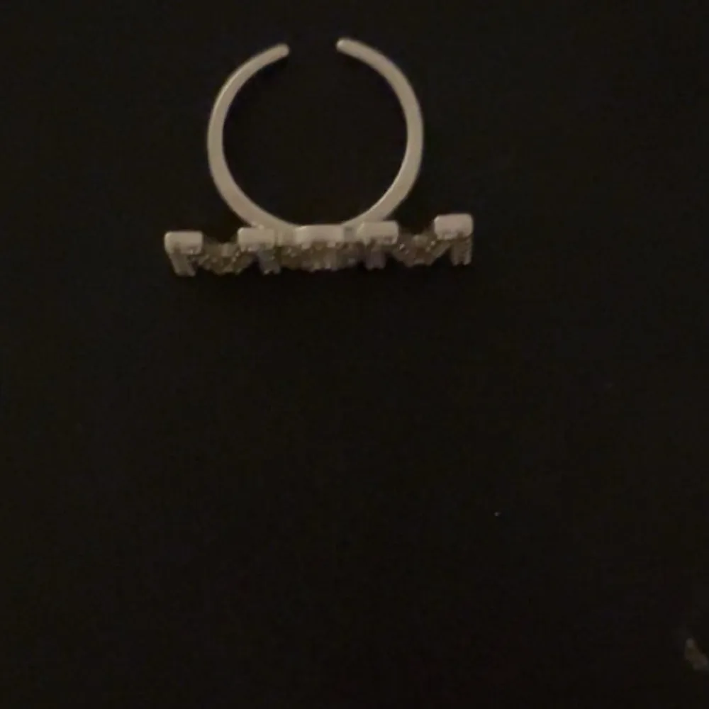 Snygg ring med texten 'MOM' dekorerad med glittrande strass. Perfekt som present till mamma eller för att visa uppskattning. Ringen har en öppen design vilket gör den justerbar i storlek. Passar till både vardag och festliga tillfällen.. Asusteet.