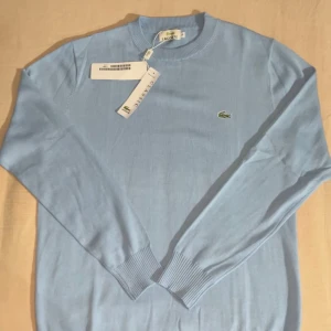 Blue Lacoste sweater *HELT NY + TAGS* - Helt ny Lacoste sweater i utmärkt skick, aldrig använd. Denna sweater kombinerar stil och komfort på bästa sätt med sin klassiska design och högkvalitativa material. Passar perfekt både till vardags och mer uppklädda tillfällen.