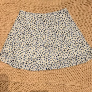 Kort sommarkjol - Söt och somrig kortkjol med blått blommönster på. Har en vit inner kjol så inget syns igenom. Finns en dragkedja på vänster sida som är dåld. Nyskick. 