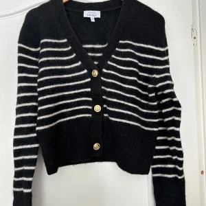 Svart och vit randig kofta från & Other Stories - Säljer en superfin svart kofta från & Other Stories med vita ränder. Den har en v-ringad design och tre snygga guldknappar framtill. Perfekt för höst och vinter, och den är både mysig och stilren. Passar perfekt till både vardag och fest! 🖤🤍