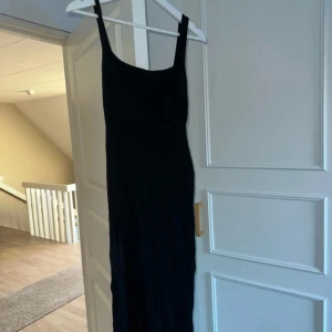 Svart långklänning - Snygg svart långklänning med smala axelband. Perfekt för en elegant kväll eller fest. Klänningen har en slits som ger en extra touch av stil. Materialet är ribbat och mjukt.