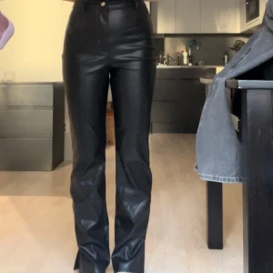 PU-byxor - Svarta PU-byxor med hög midja och slit vid foten. Väldigt bra skick, inga tecken på slitning. Storlek 36. Från missguided men köpt på nelly