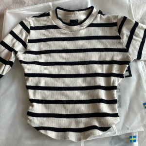 Randig ribbad tröja från Gina Tricot - Säljer en snygg randig tröja från Gina Tricot i svart och krämvit/beige. Tröjan är ribbad och har långa ärmar. Den är i storlek M men bör passa även S då den är lite mindre i storleken. Insydd midja som ni se på bilden. 😊