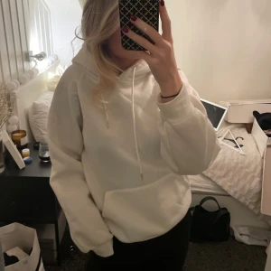 Vit hoodie - Vit hoodie med luva och dragsko. Tröjan har en stor ficka framtill och långa ärmar med ribbade muddar.