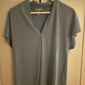 Blå blus från H&M - Säljer en stilren blå blus från H&M med korta ärmar och en v-ringad design. Har en mjuk och bekväm passform. I mycket fint skick!