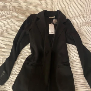 Svart kavaj från Isolde - Elegant svart kavaj från Isolde med klassisk design. Kavajen har en enkelknäppning och smickrande passform. Perfekt för att ge en stilren look till din outfit. Ny skick med prislapp