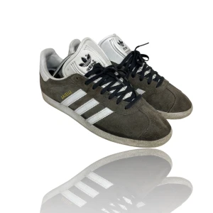 Adidas Gazelle i mocka - Snygga Adidas Gazelle sneakers i grå mocka med vita detaljer och klassiska tre ränder. Skorna har en grå snörning och en vit sula. Perfekta för en stilren look. Skick 9/10 inte så mycket använda.