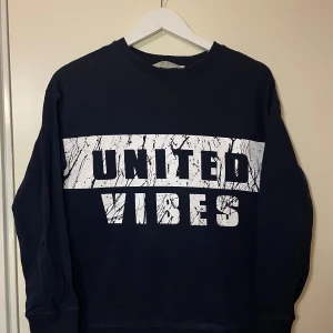  sweatshirt från H&M  - Säljer en mörkblå sweatshirt från H&M med texten 'United Vibes' i vitt och svart tryck på framsidan. Tröjan har långa ärmar och en rund halsringning. Perfekt för en avslappnad stil.