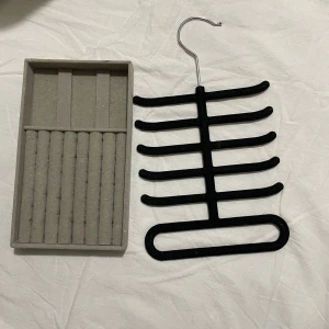 Smycken hållare  - Praktisk svart bälteshängare med flera krokar för enkel organisering av smycken . Hängaren är gjord av ett robust material och har en metallkrok för upphängning i garderoben. Perfekt för att hålla ordning på dina accessoarer.