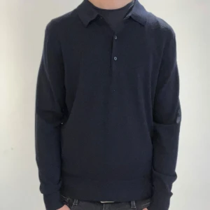 Mörkblå pikétröja från Uniqlo - Säljer en stilren mörkblå pikétröja från Uniqlo. Tröjan har långa ärmar och en klassisk krage med knappar framtill. Jag är 180cm på bilden. Djurfrit hem. 