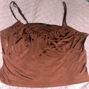 Brun topp - Säljer en brun topp från Bikbok med smala axelband och knytning framtill. Perfekt för varma dagar och kan enkelt matchas med olika outfits.