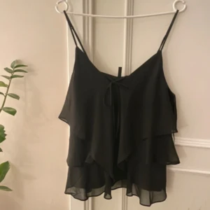 Svart ärmlös topp från Vero Moda - Snygg svart ärmlös topp från Vero Moda med volangdetaljer och knytning framtill. Aldrig använd och inga sorts defekter.